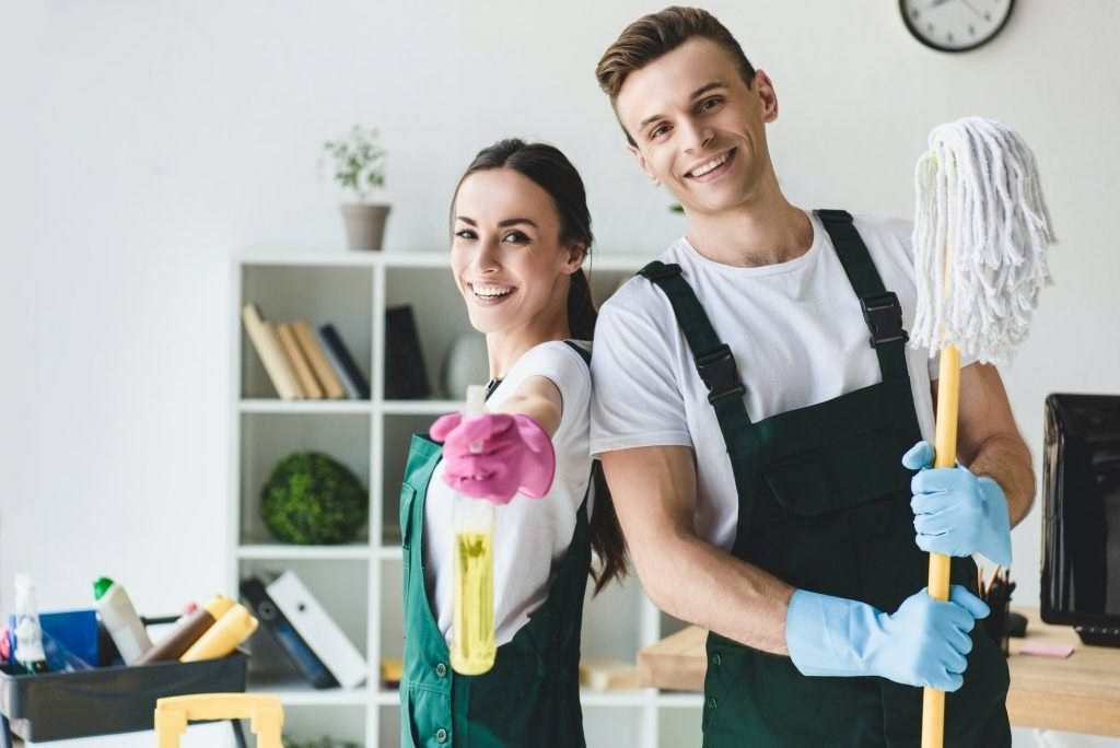 Two young cleaners with a mop and spray bottle smiling at the camera