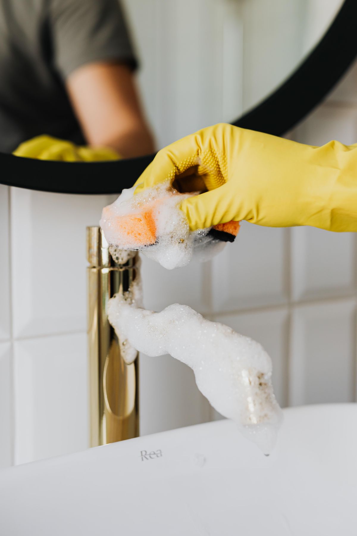 Person washing a faucet and sink wearing a yellow glove