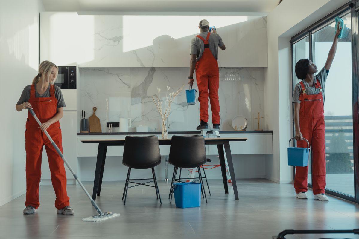 Cleaners in red uniforms mopping and wiping glass in a modern dining room